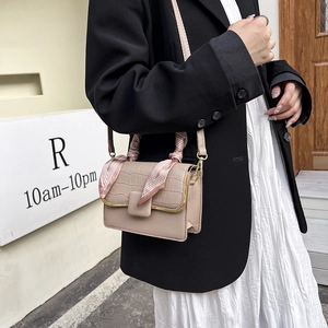 Détail du sac à rabat beige gaufré crocodile avec poignée en foulard rose sur l'épaule