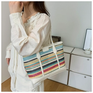 Close-up of a colorful striped woven tote bag with white leather straps on a model