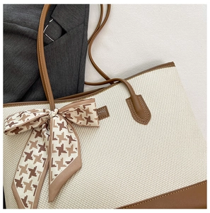 Detail of woven tote bag with brown leather trim and a houndstooth bow silk scarf