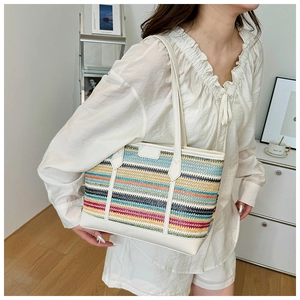 Detail of colorful striped straw tote bag featuring premium white leather trim and handles