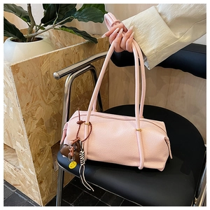 Close-up of pink cylinder shoulder bag in textured leather with a smiley face charm