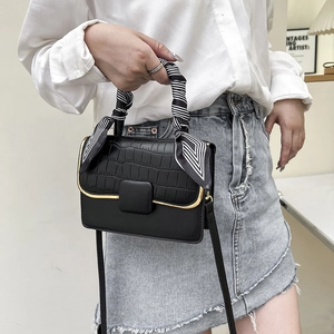 Détail du sac bandoulière noir avec garniture dorée et poignée ornée d'un foulard imprimé