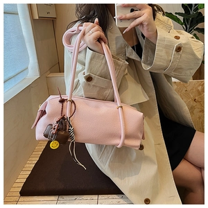 Detailed view of a pink pillow shoulder bag with a smiley charm on a slender strap