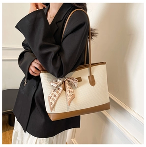 Detail of woven tote bag with brown leather handles and decorative silk bow accessory