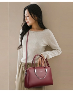 Détail d'un sac cabas rouge foncé texturé avec chaîne en argent porté par un modèle