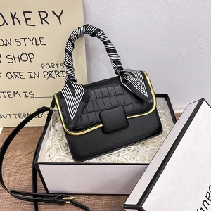 Détail d'un sac noir avec texture crocodile, foulard en soie et boîte cadeau chic