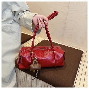 Detail of red glossy shoulder bag with a small brown charm accessory and metal zipper