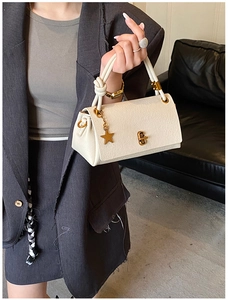 Close-up of beige lychee leather handbag with star charm and twisted handle detail