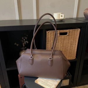 Brown litchi grain bowling tote bag with slim dual straps on a stylish display shelf