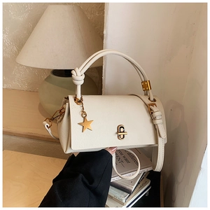Close-up of cream square handbag with gold lock and star charm on decorative books