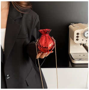 Detail of red metallic bucket bag with gold chain strap held by model in modern setting