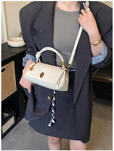 Detail of cream crossbody bag with gold star pendant and textured synthetic leather finish