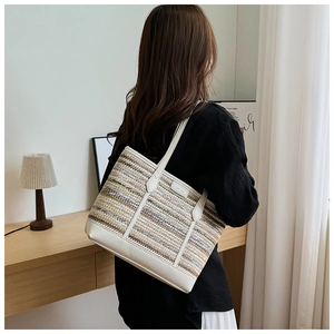 Close-up of a woven straw tote bag with white leather straps in a cozy home setting