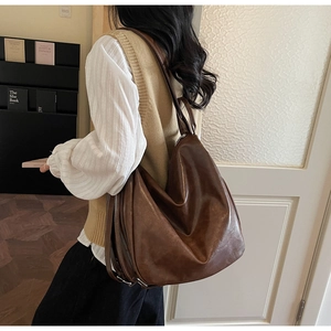 Side view of large brown faux leather tote bag worn by model in a cozy indoor setting