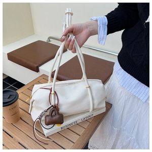 Close-up of white cylindrical shoulder bag with smooth leather and a brown charm