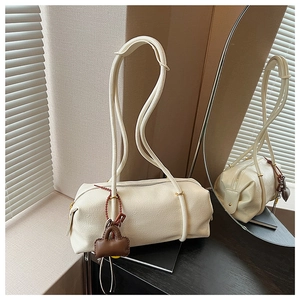 Detailed close-up of cream-white cylindrical shoulder bag with textured leather and charm