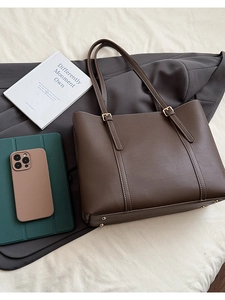 Dettaglio borsa tote marrone scuro con cuciture a contrasto e fibbie dorate regolabili
