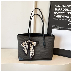 Detailed close-up of dark grey woven tote bag featuring black leather handles and silk bow