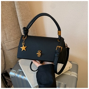 Detail of black pebbled leather handbag with gold star pendant and hardware on suit background