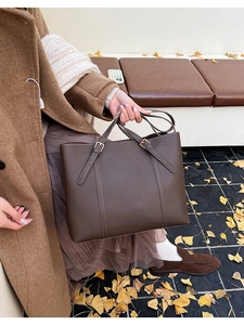 Dettaglio borsa tote in pelle marrone scuro con fibbie indossata da modella in autunno