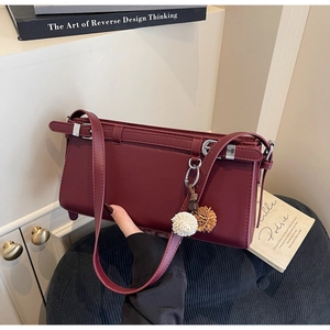 Close-up of a burgundy minimalist rectangular bag with a dual-tone fur ball pendant accessory
