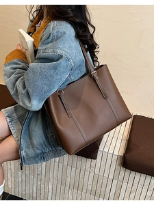 Dettaglio della grande borsa tote in pelle marrone scuro con cuciture su giacca jeans