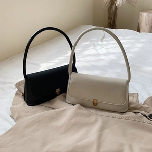 Minimalist black and beige leather handbags with long curved handles on soft bedding