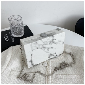 Flat lay of marble texture box clutch bag with silver chain strap on white table