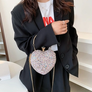 Close-up of heart-shaped glitter evening bag with gold handle and chain on a black blazer