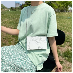 Detail of marble pattern hard shell box bag with silver metal chain on green background