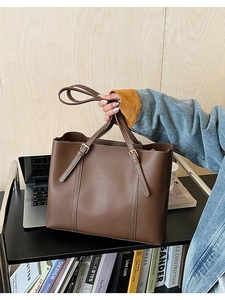 Dettaglio di una borsa tote vintage marrone scuro con cuciture bianche e fibbie metalliche