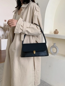 Detail of a vintage black rectangular underarm bag with a golden twist-lock on a beige coat