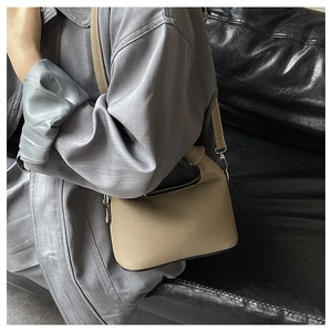 Detailed close-up of beige lychee grain leather crossbody bag with silver metal hooks