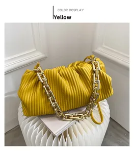 Detail of yellow pleated handbag featuring a chunky gold metal chain strap on display