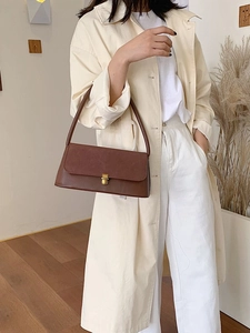 Minimalist brown leather underarm bag with vintage metal buckle worn with a beige trench coat