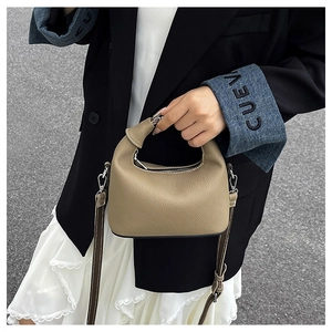 Detail of khaki pebbled leather handbag featuring silver zipper and adjustable strap