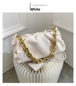 Close-up of white ruched cloud bag with bold gold chunky chain strap on textured stool