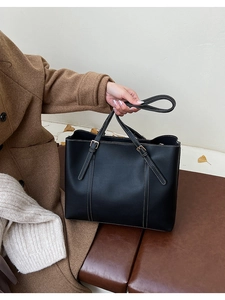 Dettaglio borsa shopper nera con cuciture bianche e fibbie dorate su sfondo autunnale