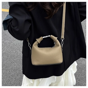 Detail of khaki lychee grain leather handbag featuring metal lock and slim strap on shoulder
