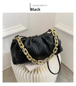 Detail of black pleated cloud pouch bag with chunky gold chain strap on white stool
