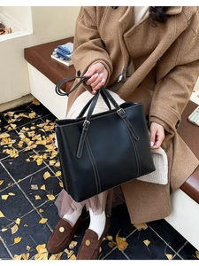 Dettaglio della borsa tote nera con cuciture bianche a contrasto in una scena di strada autunnale