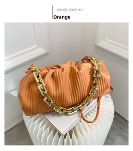 Close-up of orange pleated cloud bag with chunky gold chain on minimalist pedestal