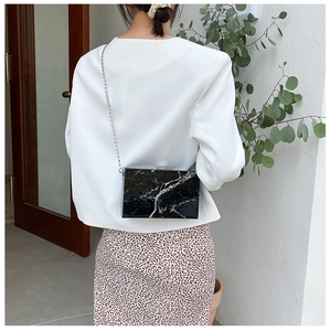 Detail of black marble pattern box bag with silver metal clasp and thin chain strap