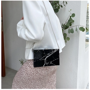 Chic black marble acrylic box clutch featuring a silver chain strap shown on a model