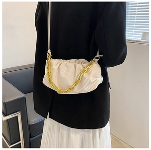 Detail of a beige ruched cloud bag with a chunky gold chain strap worn by a model