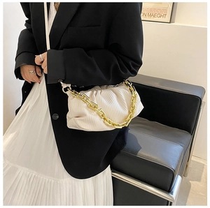 Detail of white pleated cloud bag with chunky gold chain strap worn by a stylish model