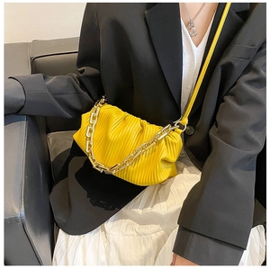 Detail of yellow pleated cloud bag featuring a bold chunky gold chain and leather texture