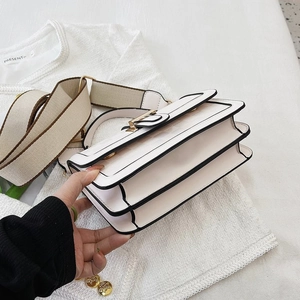 Detail view of structured white crossbody bag with black piping and three compartments
