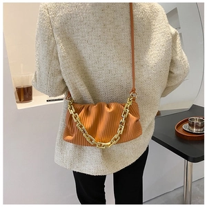 Detail of a pleated orange-brown cloud bag with bold gold chain on a tweed jacket
