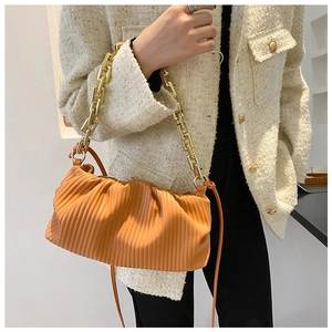 Detail of orange pleated cloud bag with chunky gold chain strap and textured leather finish